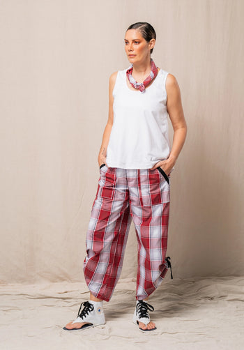 Woman wearing a white sleeveless top and red plaid pants against a beige background