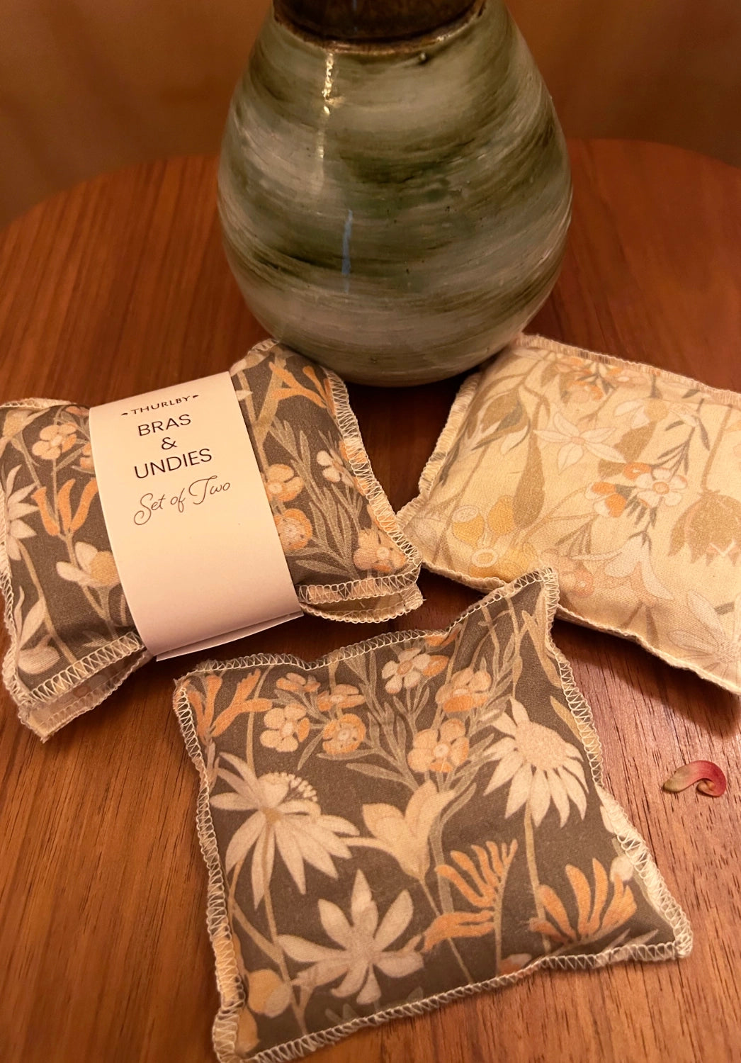 Floral-patterned aromatics on a wooden surface with a vase in the background
