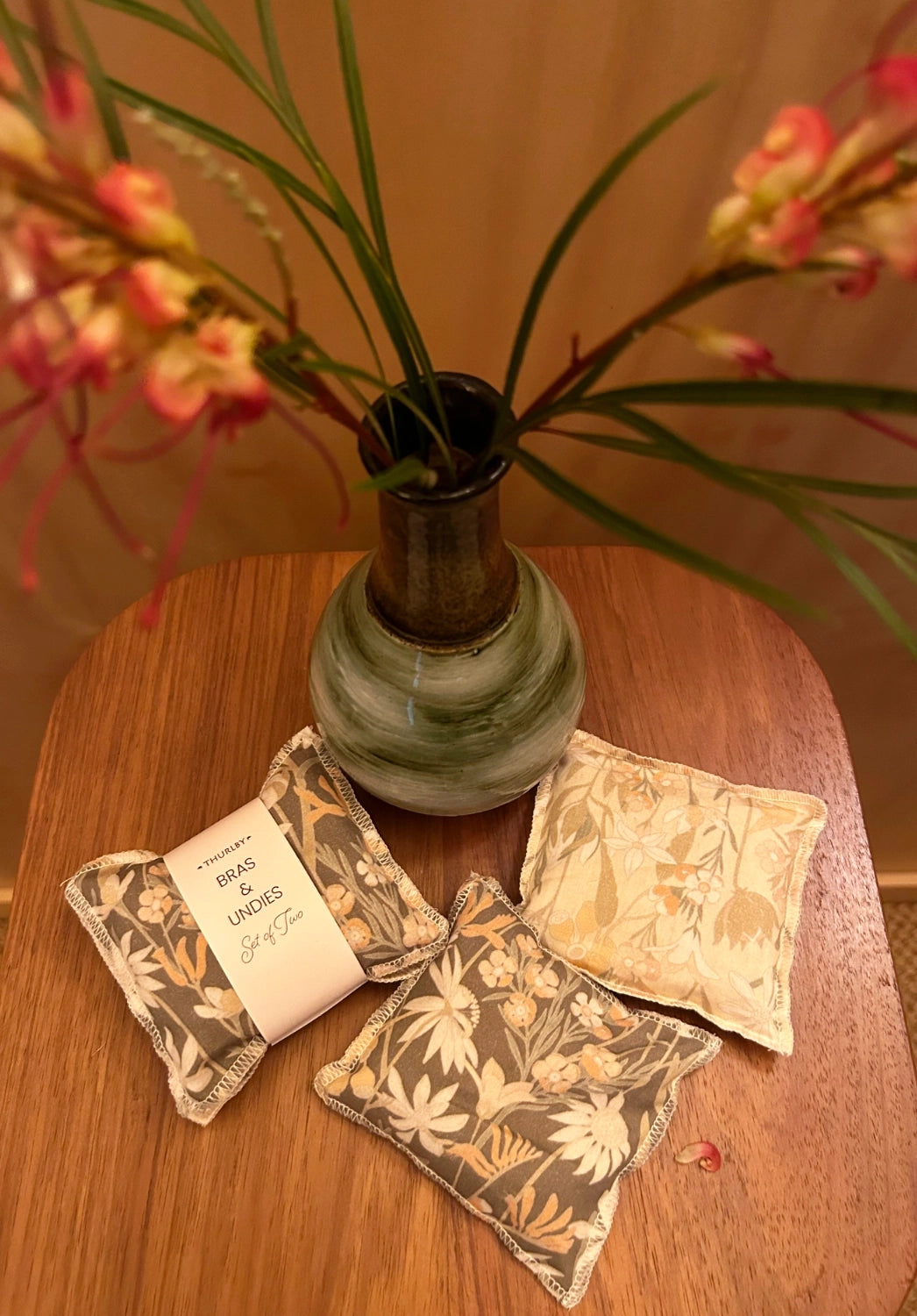 Decorative pillows with floral patterns on a wooden table with a vase of flowers in the background.