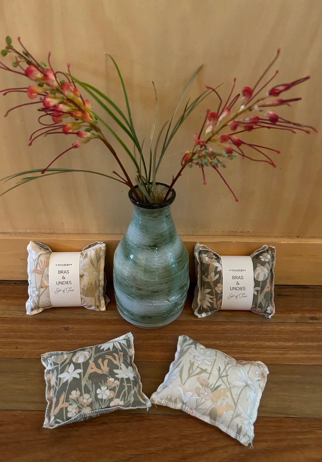 Decorative pillows with floral patterns and a vase with flowers on a wooden surface.