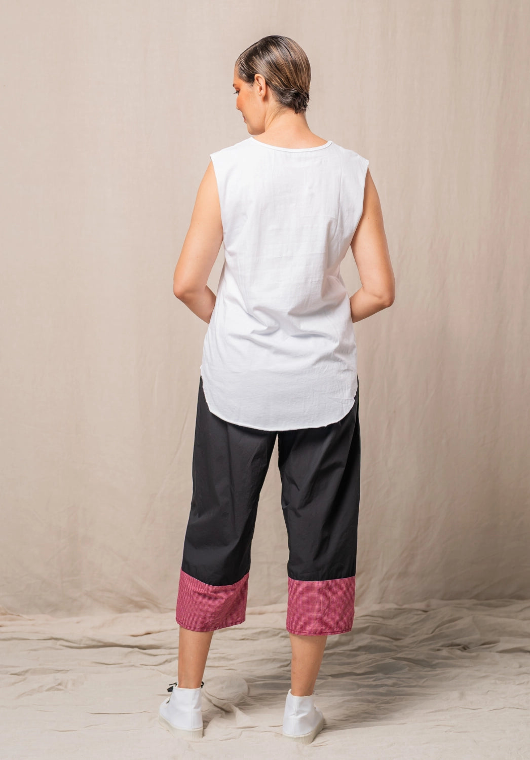 Woman wearing a white sleeveless top and black pants with red checkered cuffs against a beige background