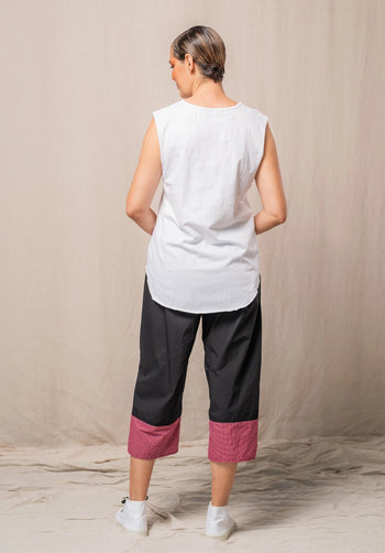 Woman wearing a white sleeveless top and black pants with red checkered cuffs against a beige background