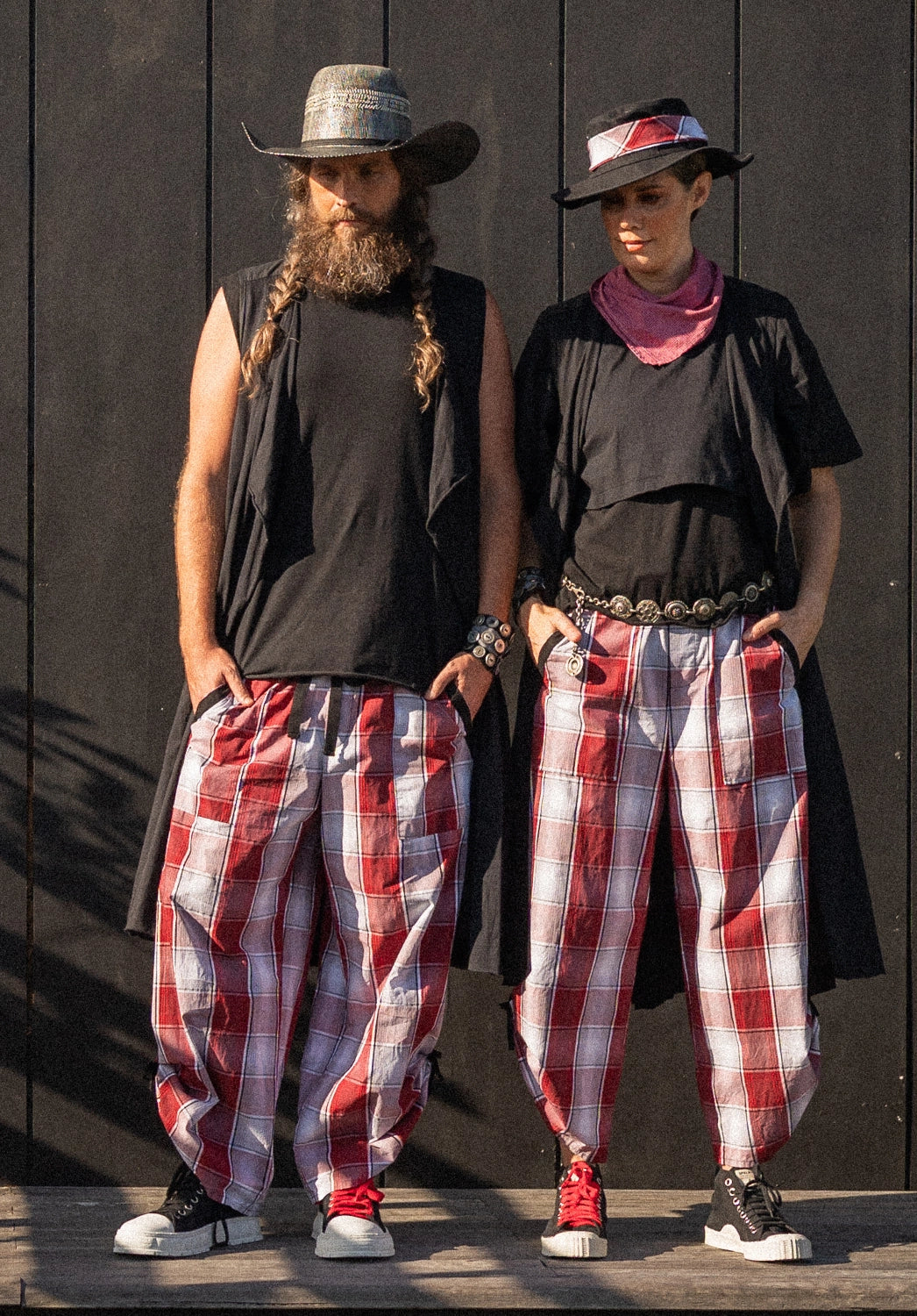 Two people wearing matching outfits with plaid pants and hats against a dark background