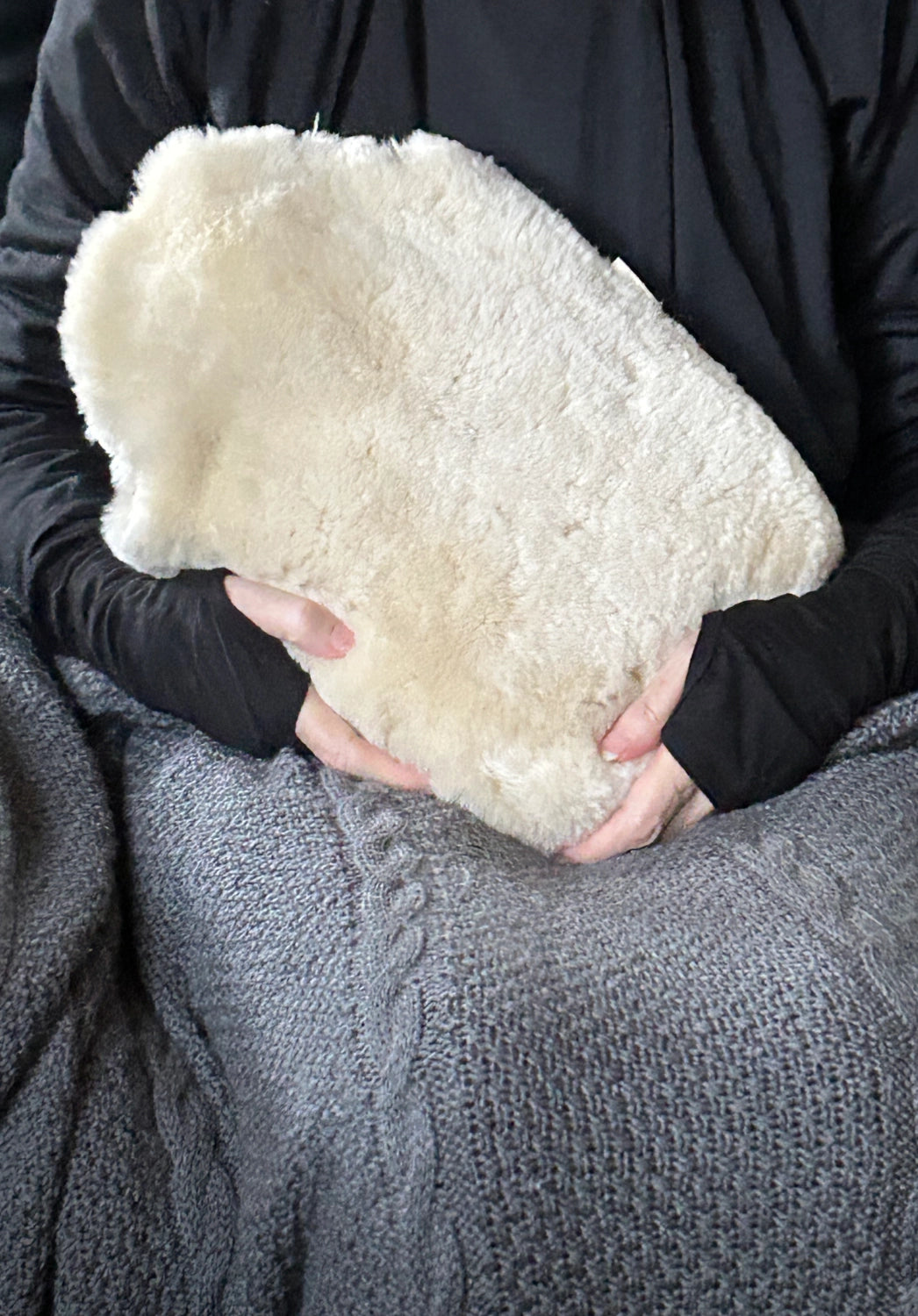 Person holding a white sheepskin hot water bottle against a dark background