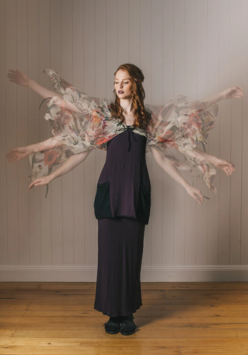 Woman with floral wings standing against a plain wall.