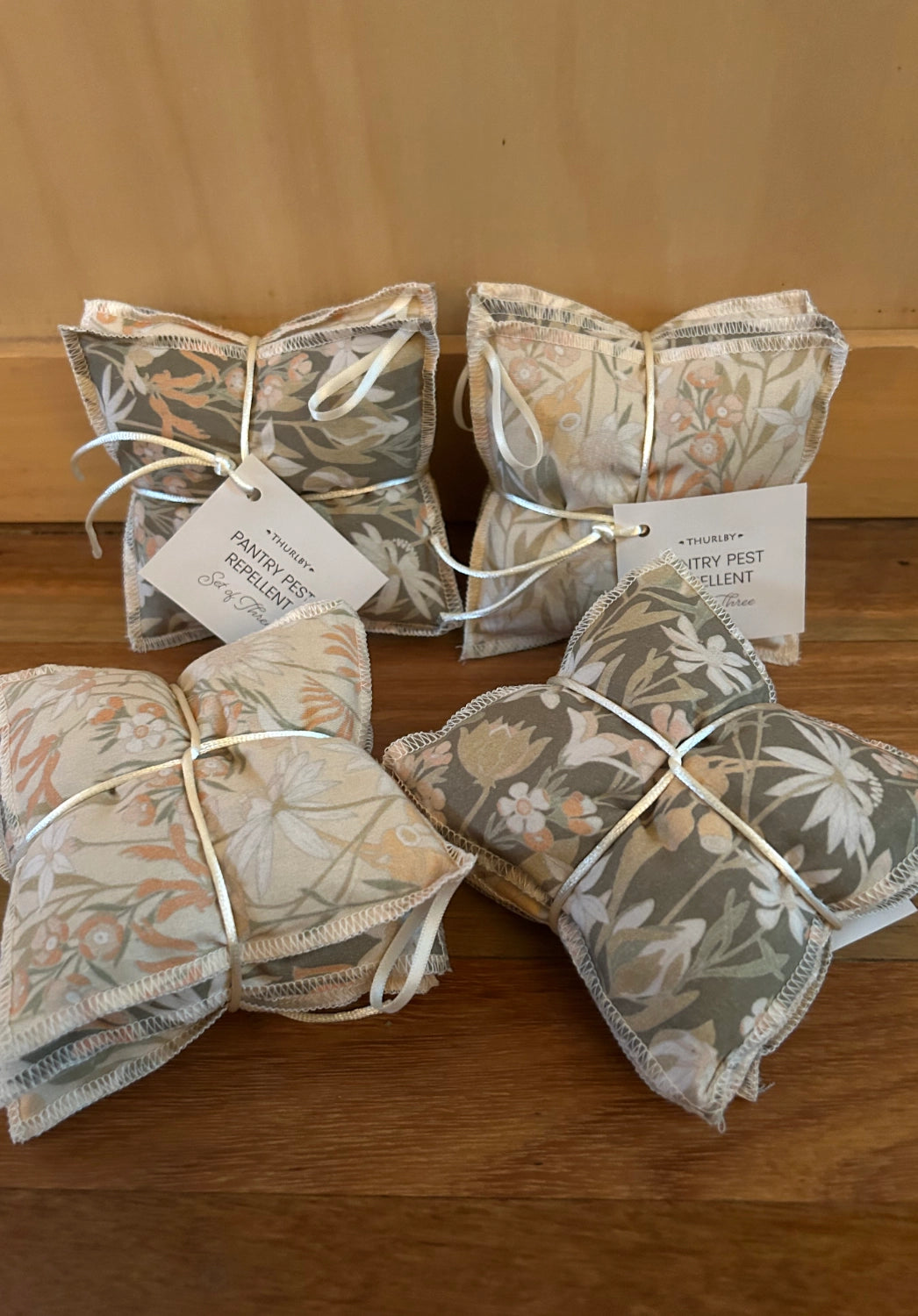 Packets of natural pest repellent on a wooden surface with a vase of flowers in the background.