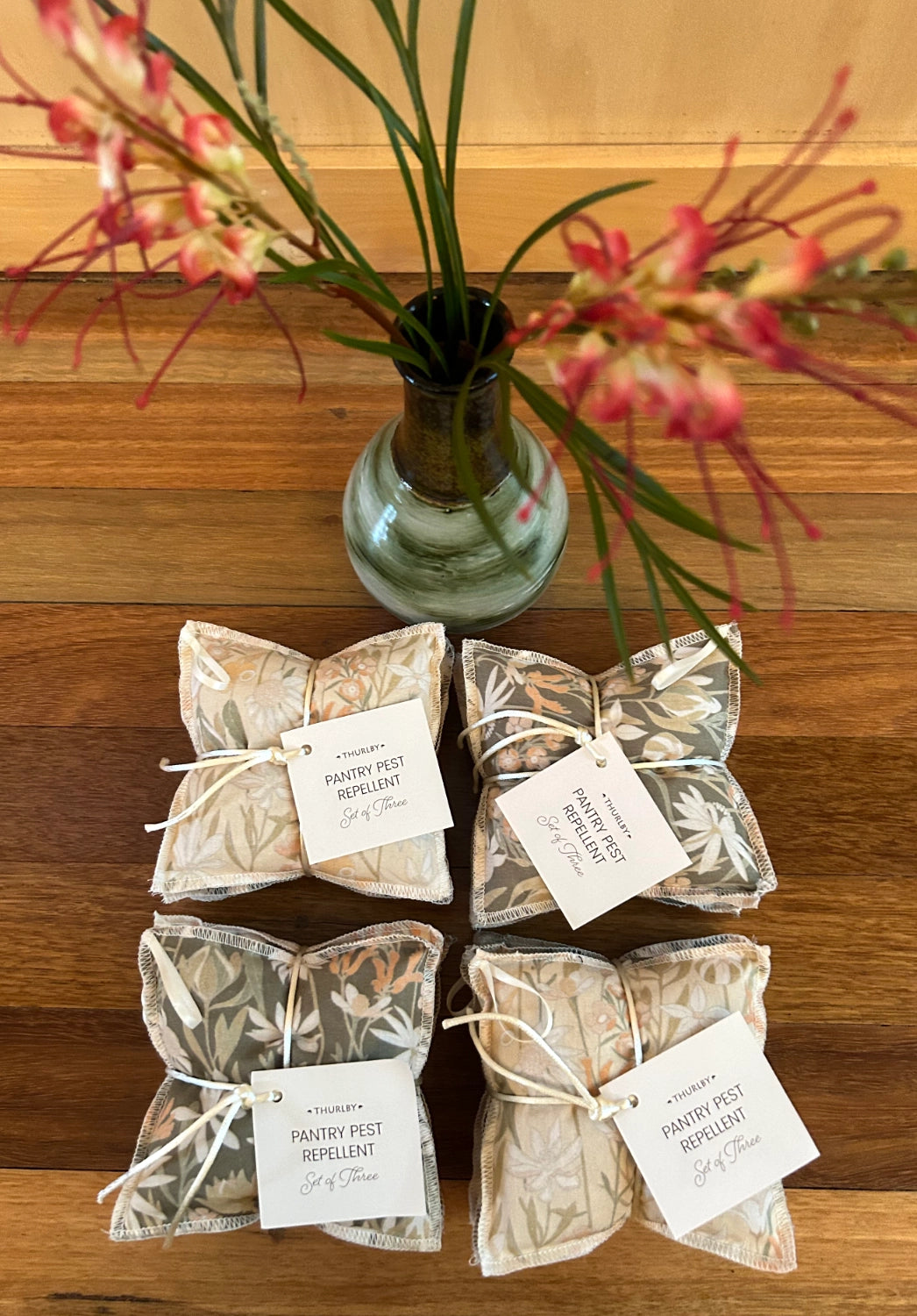 Packets of natural pest repellent on a wooden surface with a vase of flowers in the background.