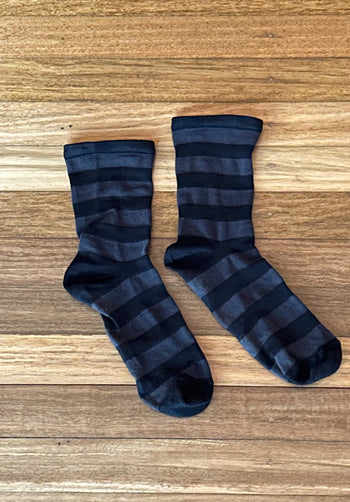 A pair of dark navy and charcoal gray striped crew socks laid flat on a light brown wooden surface.