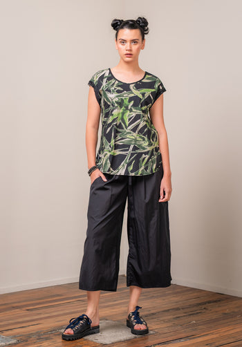 Woman wearing a black and green leaf-patterned top with black pants on a plain background