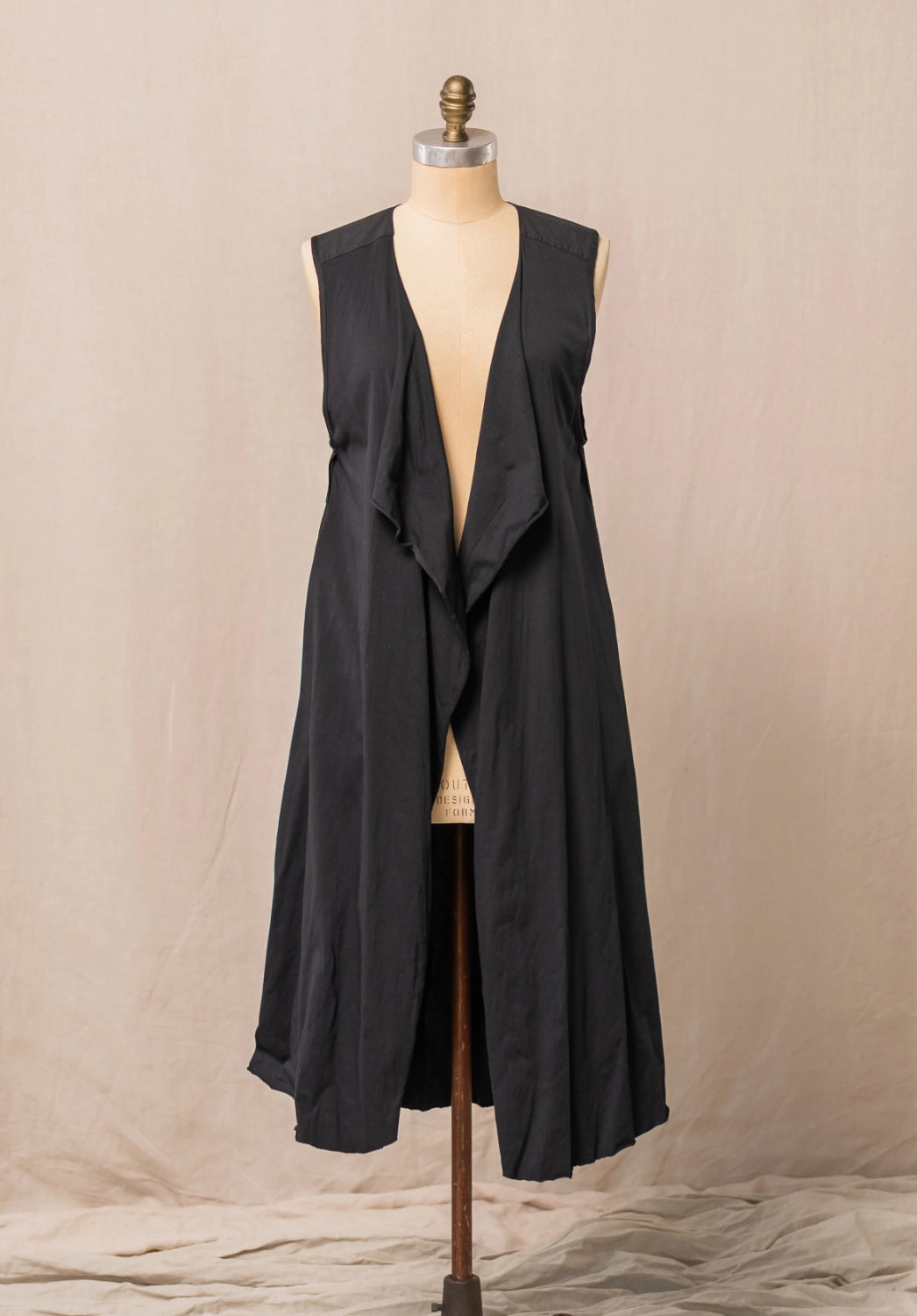 Black sleeveless long vest on a mannequin against a beige background
